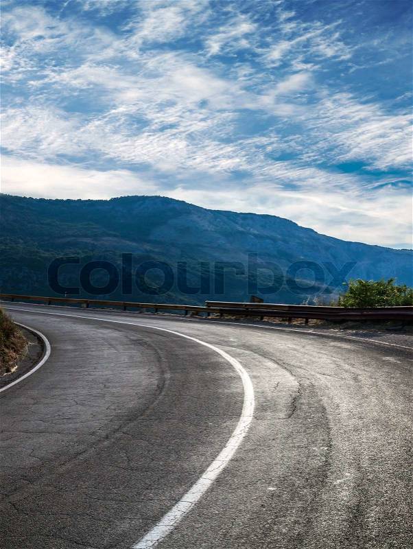 Turning rural road with blue mountains and cloudy sky on a background, stock photo