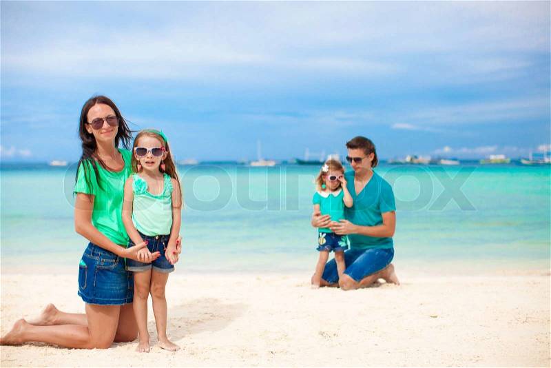 Mom with her older daughter in the foreground and dad with youngest daughter in the background on the beach, stock photo