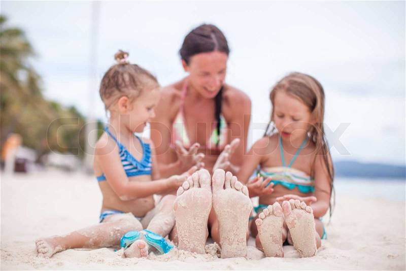 Close-up of the feet of mother and two daughters on the white sandy beach, stock photo