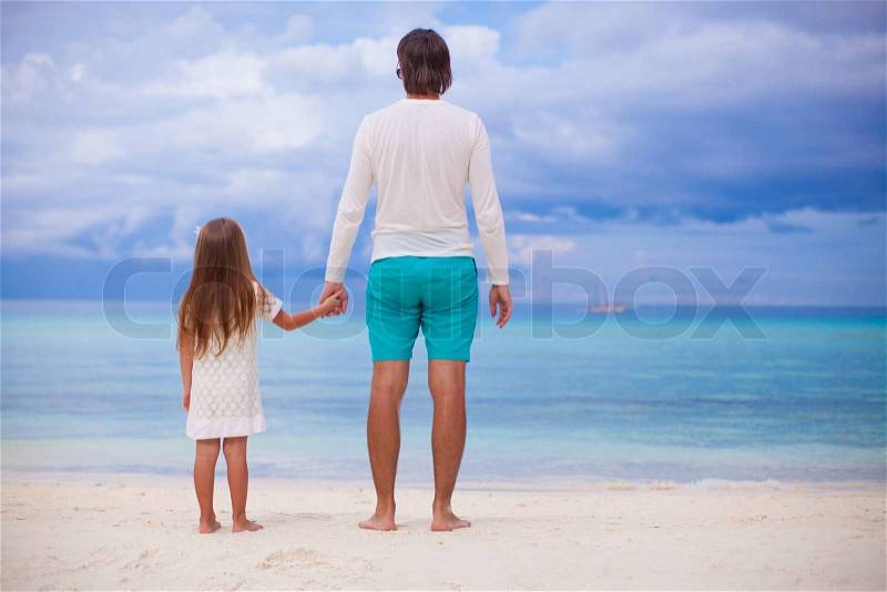 Back view of little girl hugging with dad on the beach, stock photo