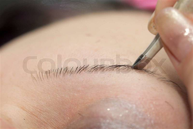 Beautician tweezing woman eyebrows in a spa center, stock photo