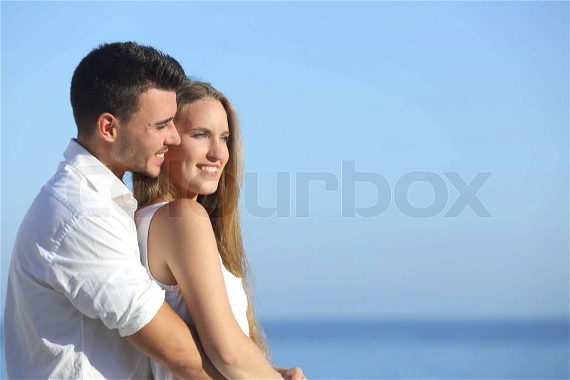 Attractive couple flirting and cuddling looking ahead with the sea in the background, stock photo