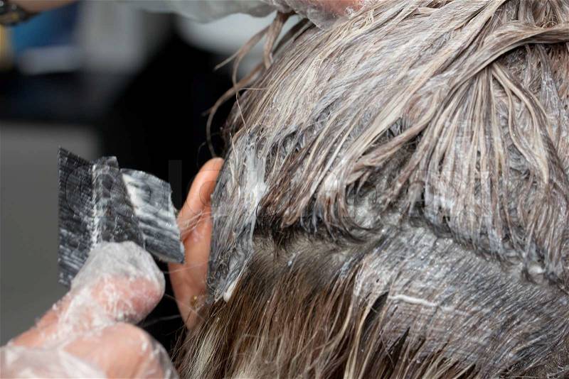 Beautician applying hair dye on female customer's hair, stock photo