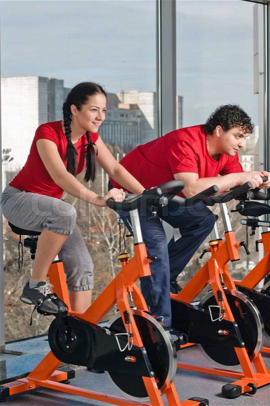 Young man and woman on exercise bicycle in fitnesss hall, stock photo