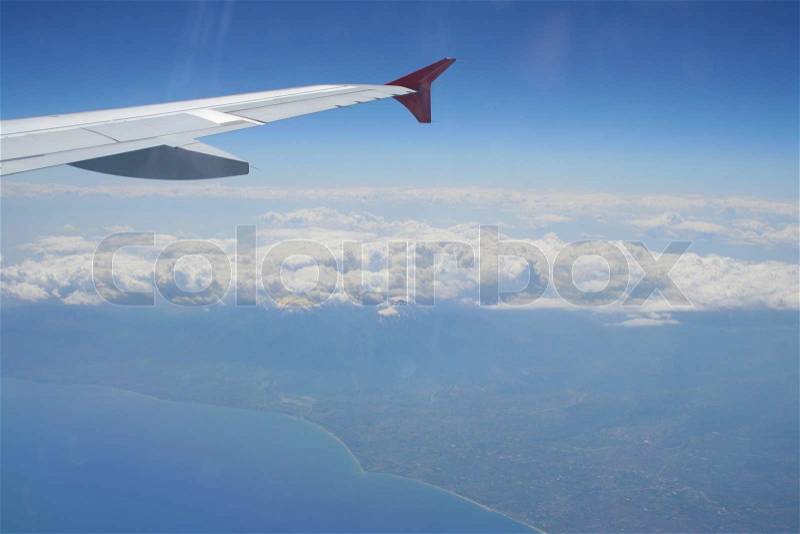 View of jet plane wing with land and sea below, stock photo