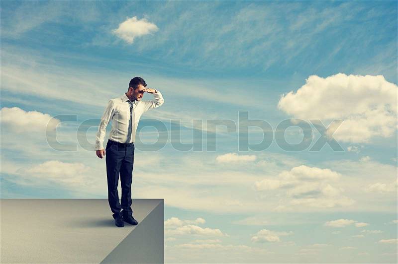 Young businessman standing on the edge and looking down, stock photo