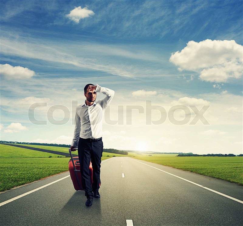 Tired young businessman with suitcase walking on the road, stock photo