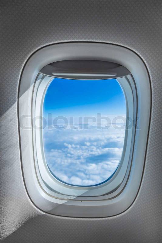 Aircraft Window with plane cruising against bright blue sky and clouds, stock photo