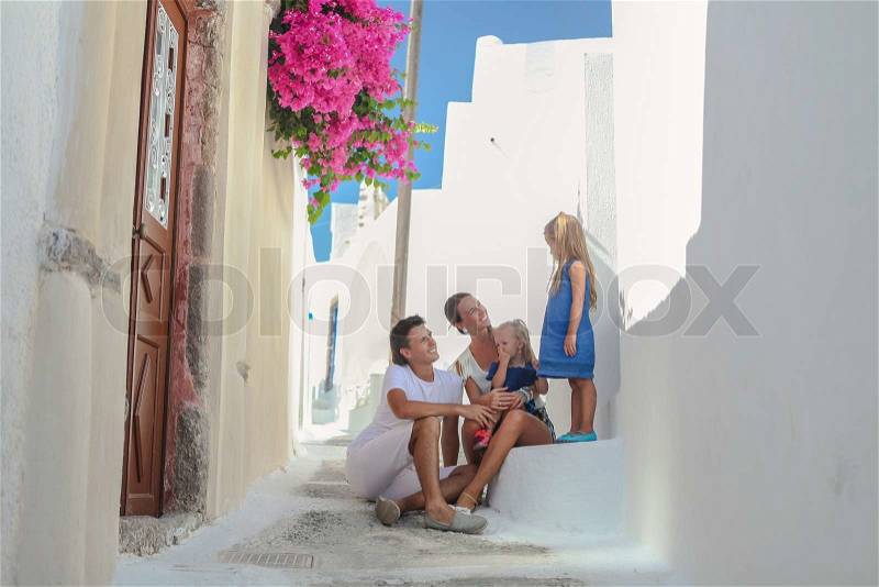 Beautiful family of four sitting on doorstep at old greek house in the street Emporio,Santorini, stock photo