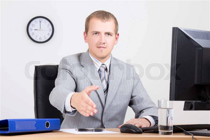 Young businessman offering a welcoming hand in office, stock photo