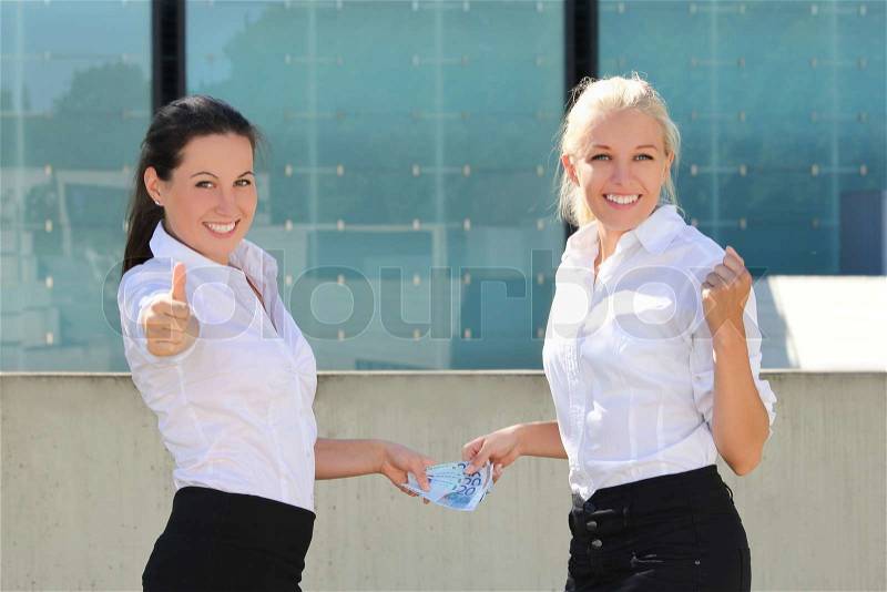 Two business women thumbs up with euro banknotes over street background, stock photo