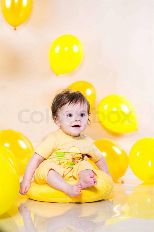 Baby sitting on the cushion with yellow balloons, stock photo