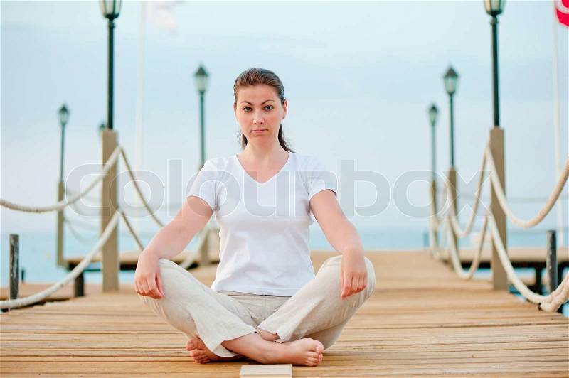 Beautiful girl in lotus position resting on the pier at the sea, stock photo