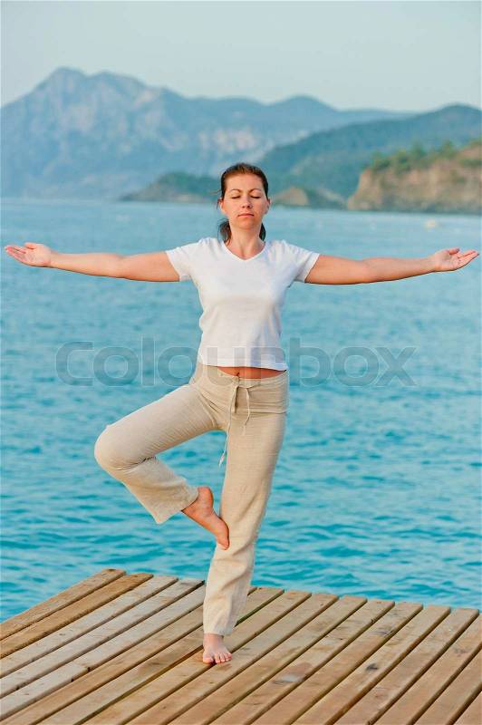 Girl by holding a balance while standing on one leg on pier, stock photo