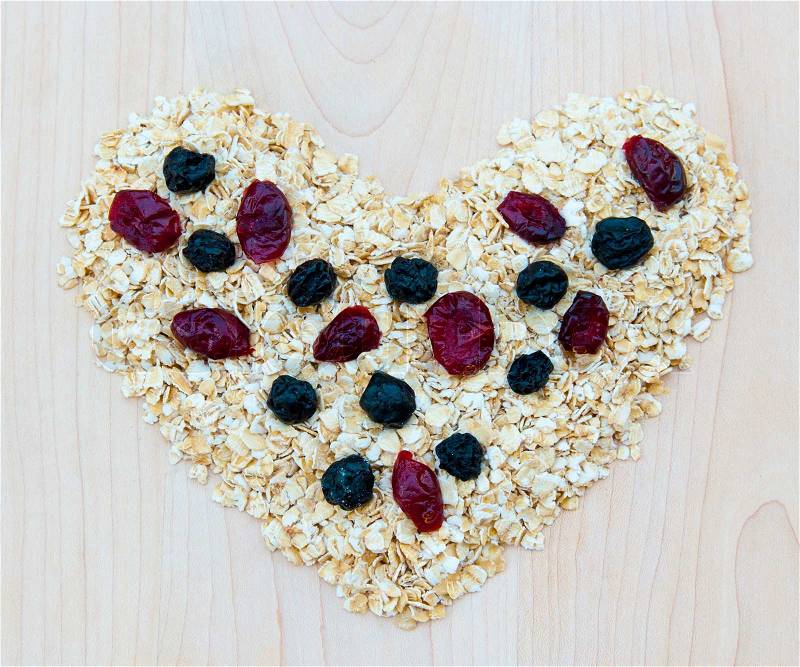 Whole grain oats with dried cranberries and blueberries in heart shape on wooden board, healthy food, stock photo