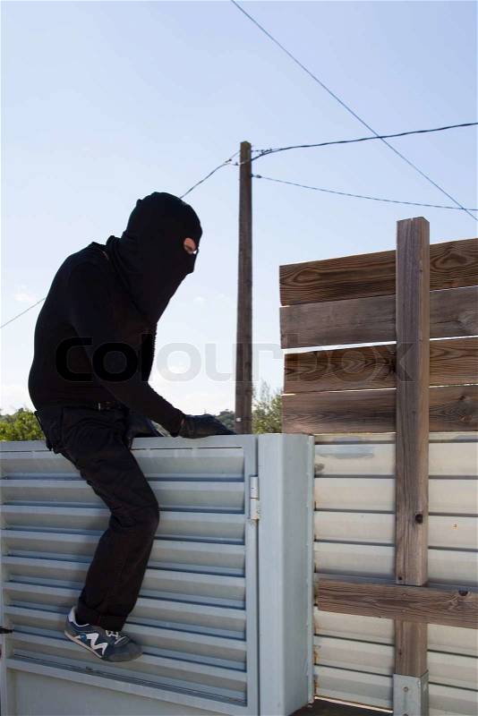 Thief jumping the fence of a private home, stock photo
