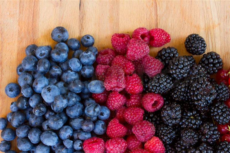 Ripe of fresh raspberry, blackberry and blue berry on wooden table, stock photo