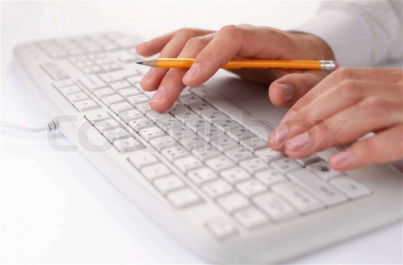 Man typing on a computer keyboard at work holding a pencil in the fingers of one hand as he enters data, close up view, stock photo