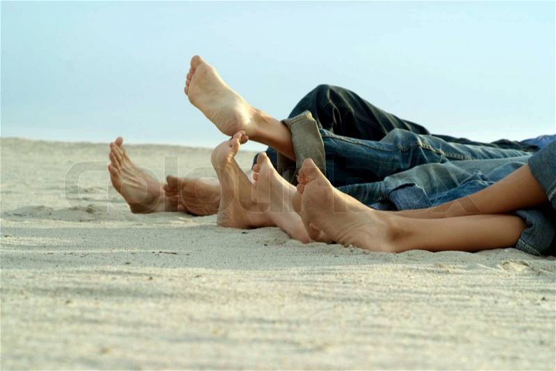 Feet four people lying on light sand, stock photo