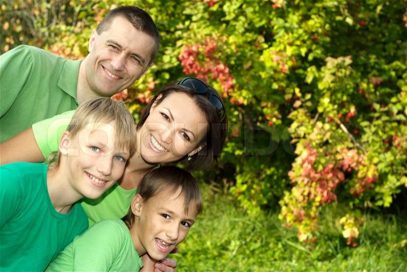 Happy family in green shirts walking in the summer park, stock photo
