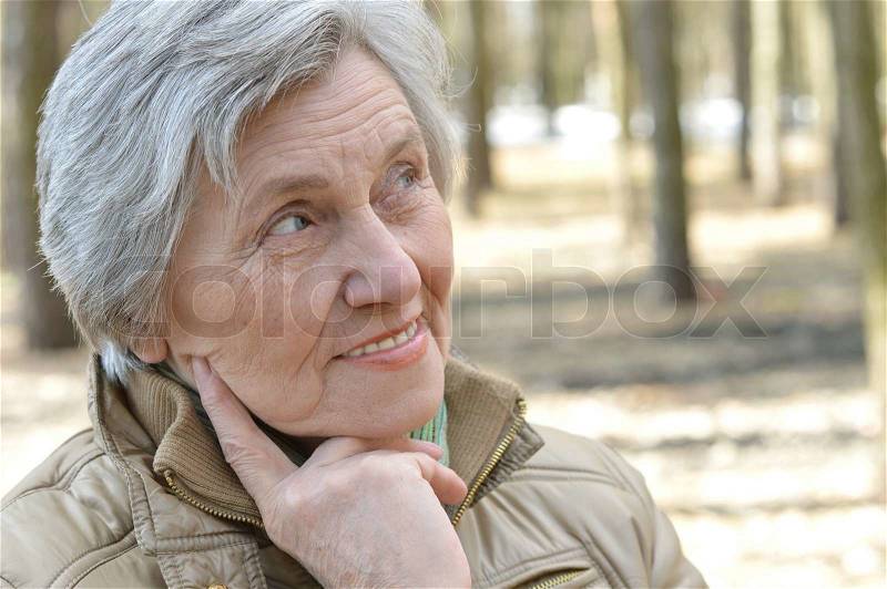 Pensive elder woman walking in the forest in autumn, stock photo