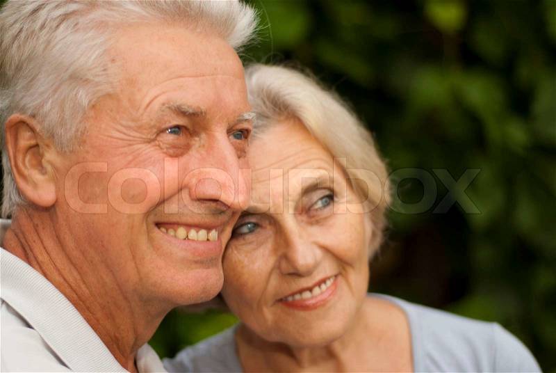 Nice elderly couple in the garden on a background of green trees and bushes, stock photo