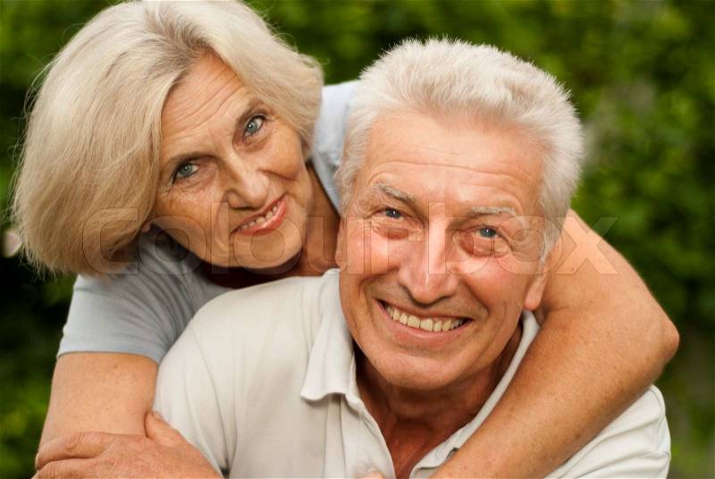 Nice elderly couple in the park on a background of green trees and bushes, stock photo