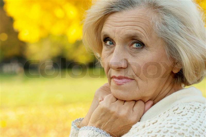 Beautiful old woman stands on a background of yellow leaves, stock photo