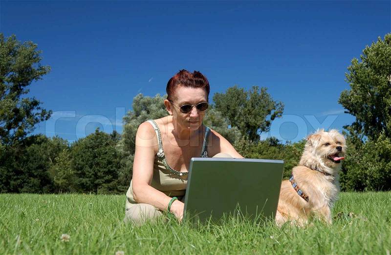 Senior woman with laptop and dog in a park, stock photo