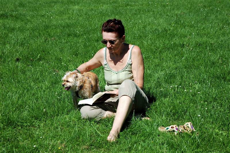 Lady reading in a book and playing with her dog, stock photo