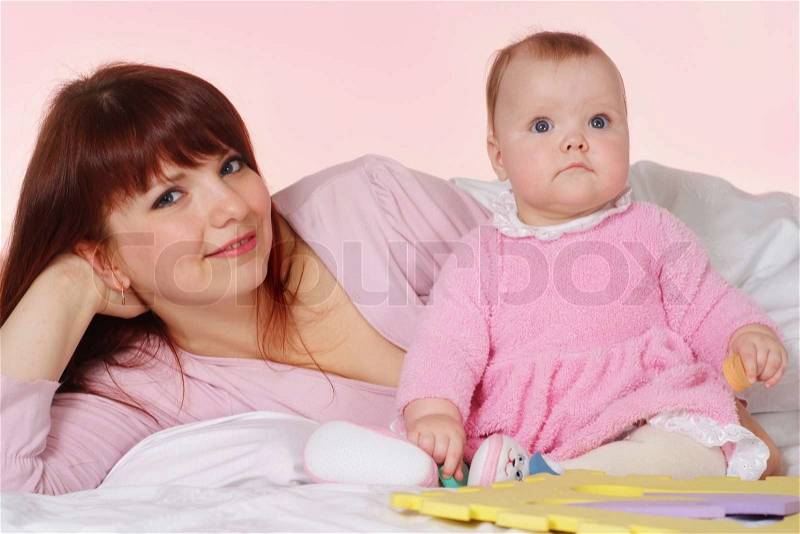 A beautiful nice mother with her daughter lying in bed on a light background, stock photo