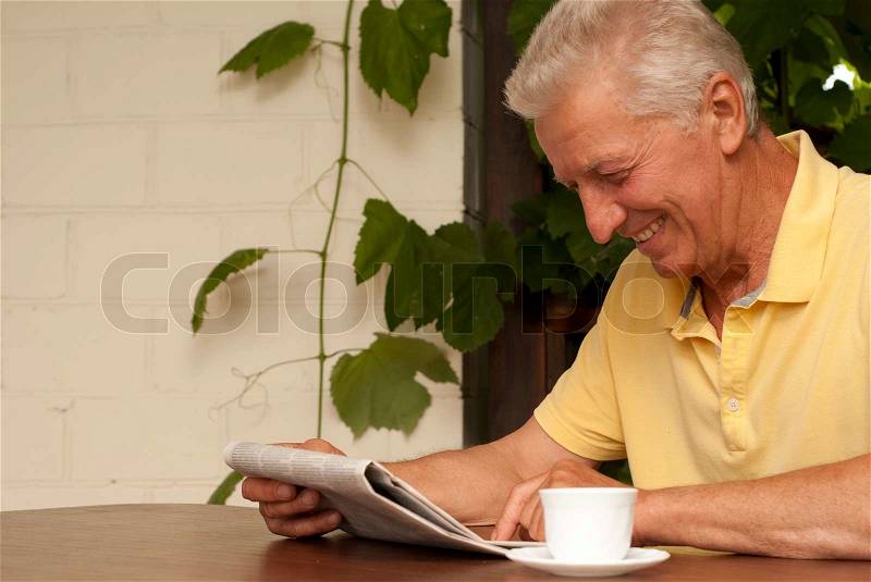 Attractive older man sitting at a table at home on the veranda, stock photo