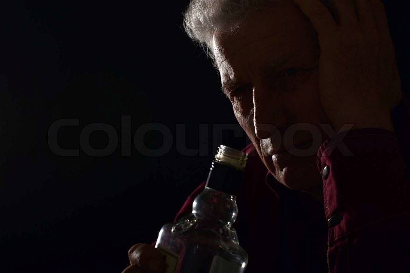 Lonely old man drinking alcohol on a black background, stock photo