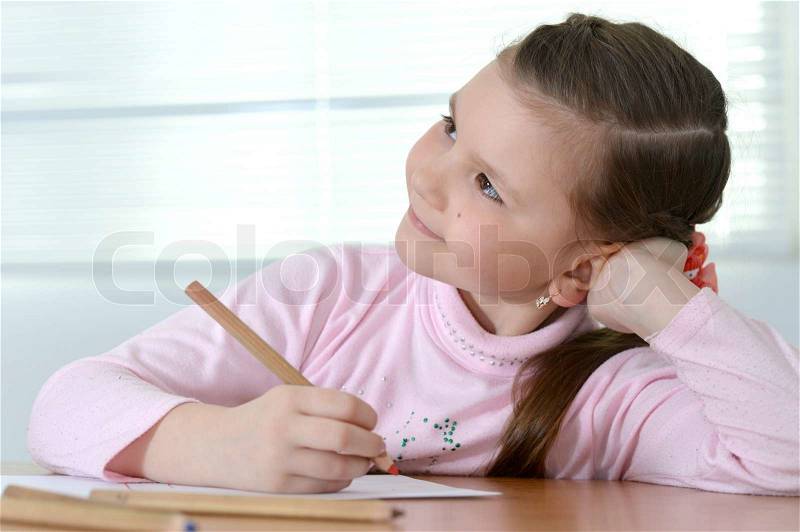 Young pretty girl in a pink sweater drawing at the table at home, stock photo
