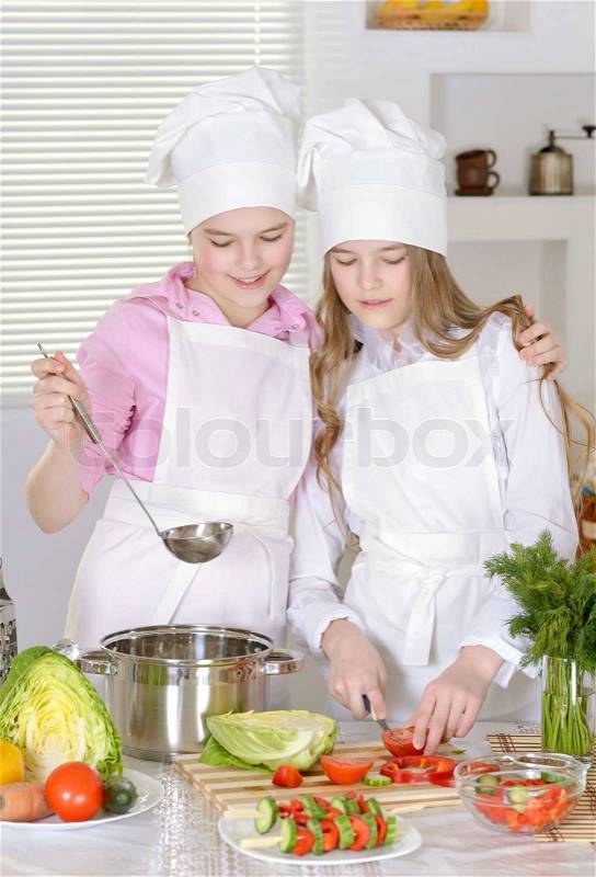 Two cheerful teen girls preparing dinner in the kitchen at home, stock photo