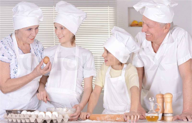 Elderly couple and their grandchildren kneading the dough for the cake together, stock photo