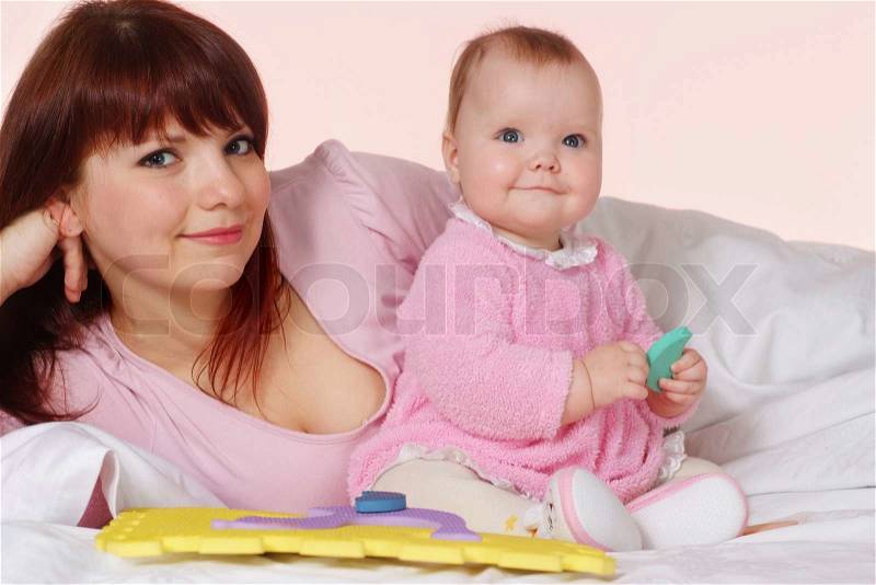 A beautiful pretty mother with her daughter lying in bed on a light background, stock photo