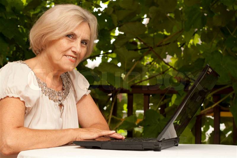 Sweet older woman sitting at a table at home on the veranda, stock photo