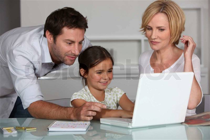 Young girl using a laptop computer with her parents, stock photo