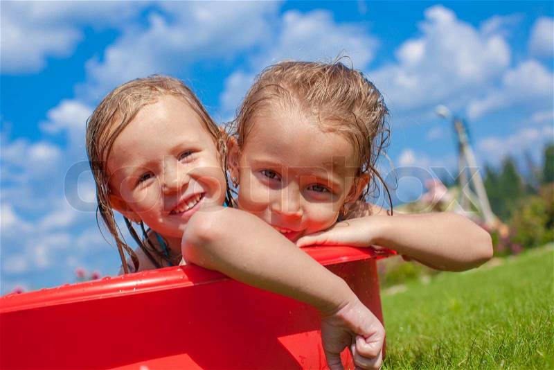 Two cute little happy girls having fun in small pool on the courtyard outdoor, stock photo