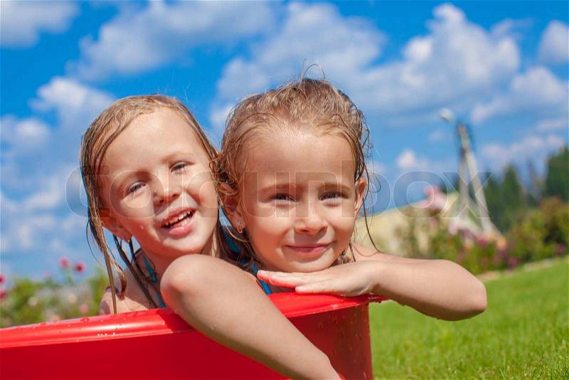 Two cute little happy girls having fun in small pool on the courtyard outdoor and enjoy their vacation, stock photo