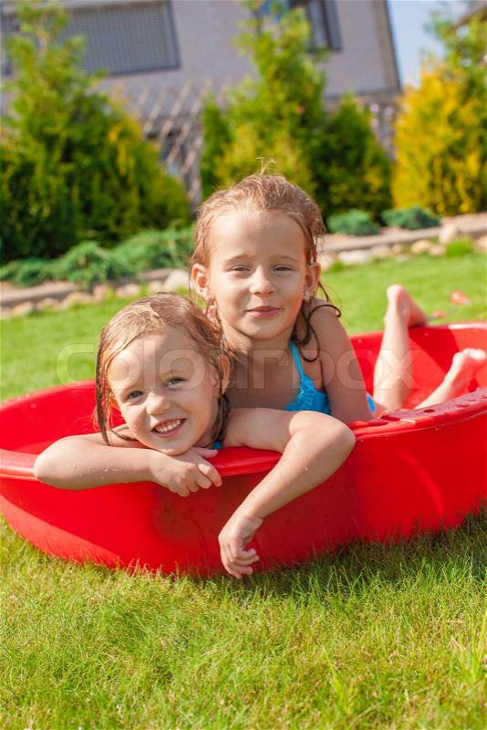 Two cute little happy girls having fun in small pool on the courtyard outdoor and enjoy their vacation, stock photo