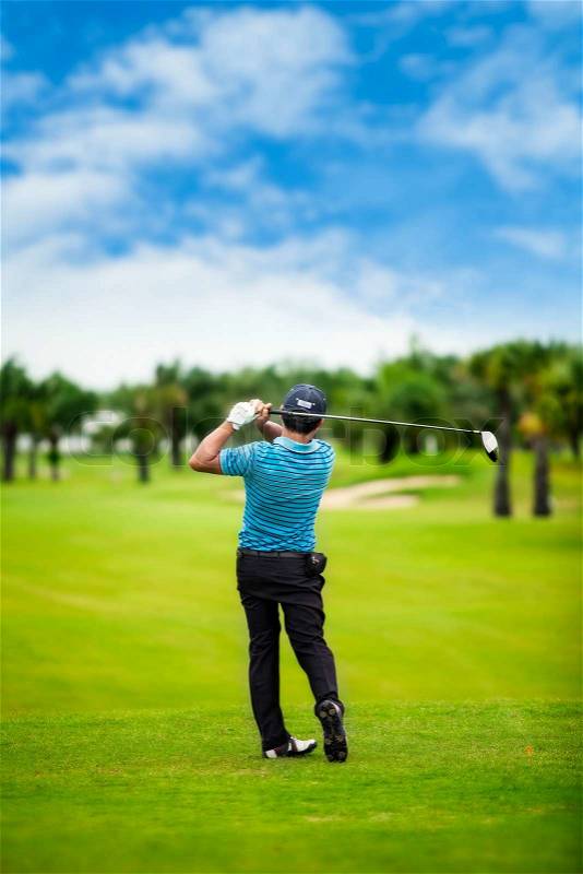Male golf player teeing off golf ball from tee box, wonderful cloud formation in background, stock photo