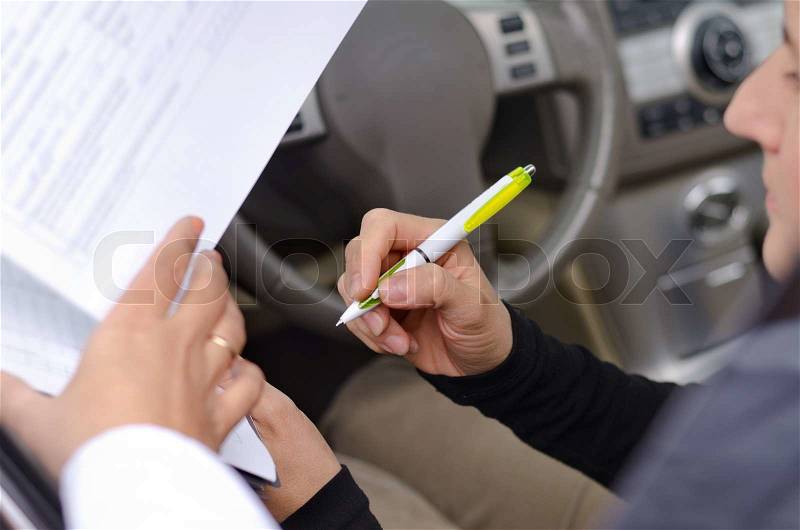 Woman driver signing paperwork for the purchase or insurance on a new vehicle, stock photo