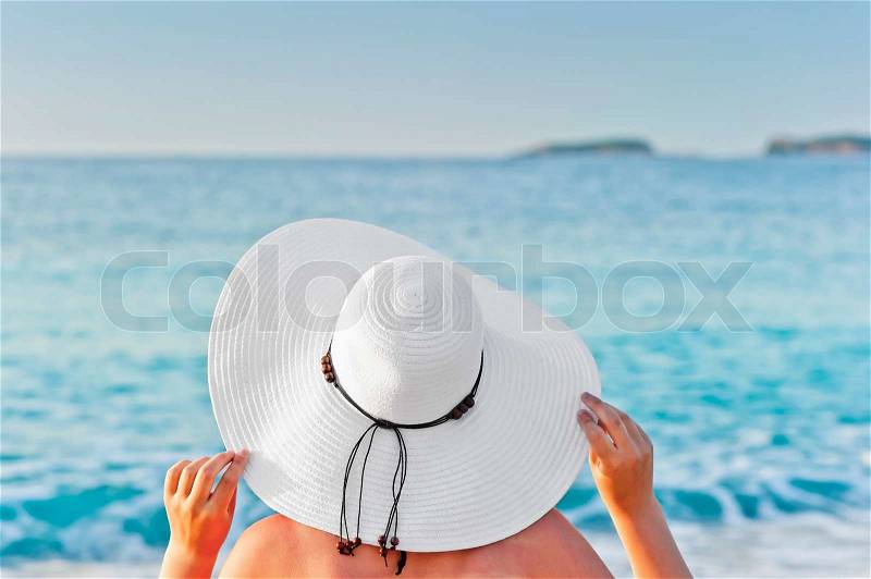 A woman sunbathing on a deck chair on the beach and holding hands hat, stock photo