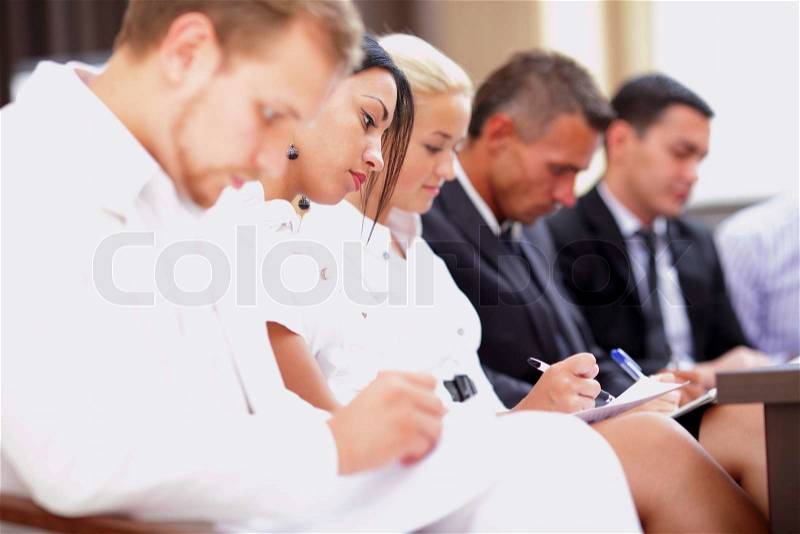 Business people sitting in a row at meeting and making notes. Focus on woman, stock photo
