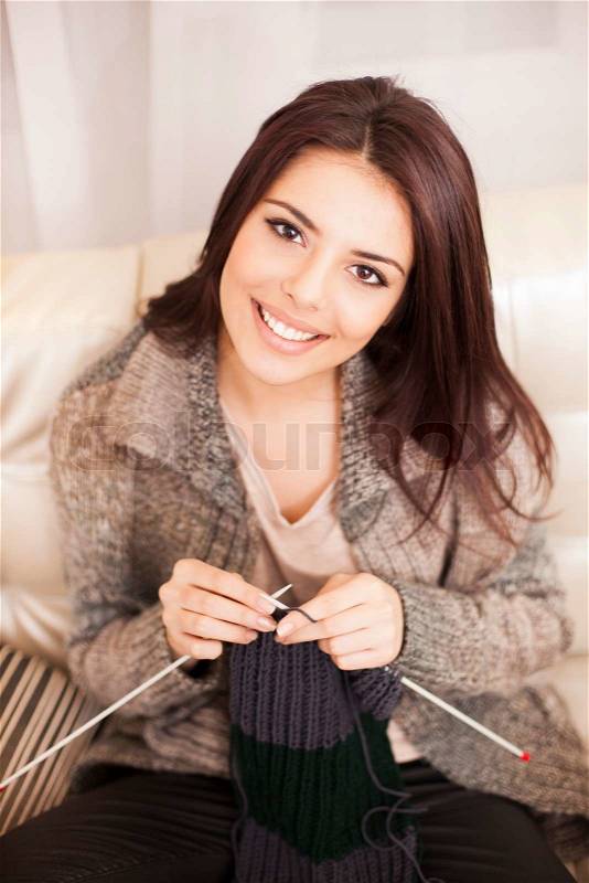 Young woman knitting a scarf and smiling, stock photo