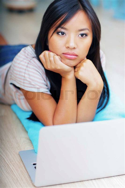 Dreamy young asian woman lying on the floor with laptop, stock photo