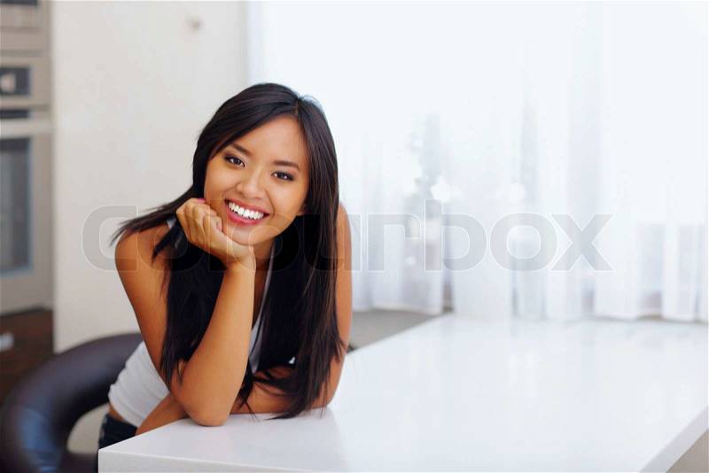 Happy beautiful asian woman leaning on hand in her kitchen, stock photo