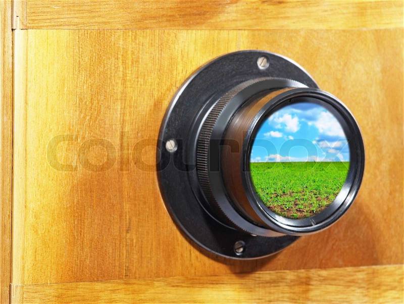 Old camera lens with blue sky and green grass inside, stock photo